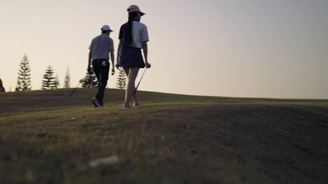Couple Golfing player talking about nice shot in golf course after hit the golf ball to hole for score, sports relax in holidays summer vacation at sunset golden time, cinematic UHD 4k footage