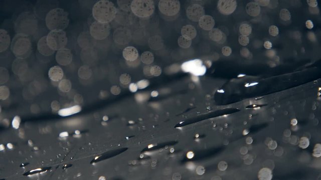Narrow streamlet of rainy water flowing among bursting drops in slow motion