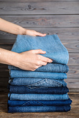 Woman folding stylish jeans on wooden table, closeup