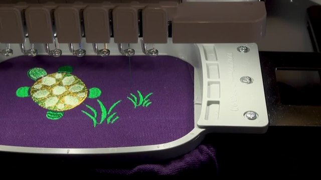  work of the embroidery machine with the green  thread  when performing work on the automated production of a colored design grass and turtle  on the purple background