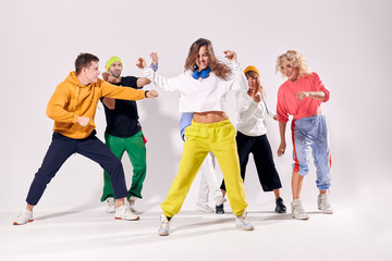 Beautiful lady with long curly hair dressed in bright yellow pants and white t shirt dancing with passion, focused on training modern dance movie, having joyful friends behind