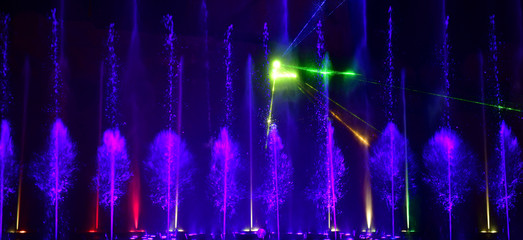 Colorful water fountains. Beautiful laser and fountains show. Large multi colored decorative dancing water jet led light fountain show at night. Dark background.