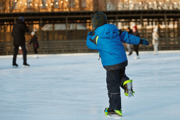 The boy is skating at the rink. The child learns with his parent to ice skate.