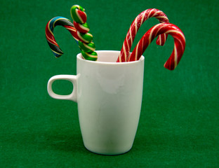 Obraz na płótnie Canvas White Cup with Christmas candies on a green background.