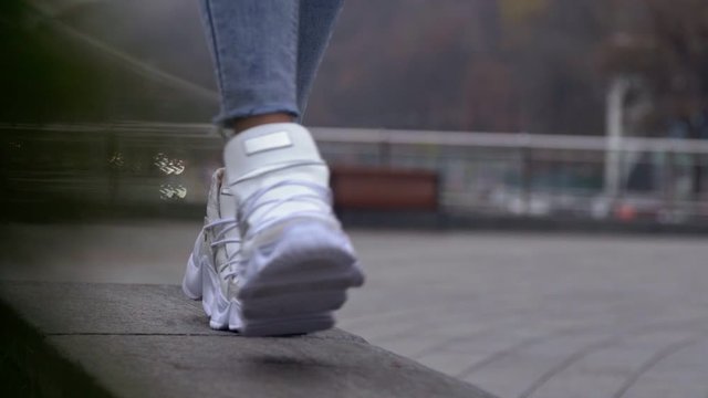 Closeup of girl in white sneakers staps up on parapet and then walks