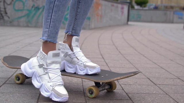 Girl in white sneakers stands on skateboard