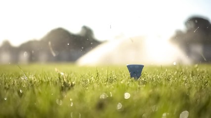 Golf club hits a golf ball in a super slow motion. Drops of morning dew and grass particles rise into the air after the impact.