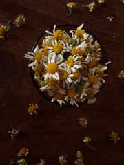 Bowl color ambar transparente con flores de manzanillas frescas, sobre un fondo rustico de madera. Top View.