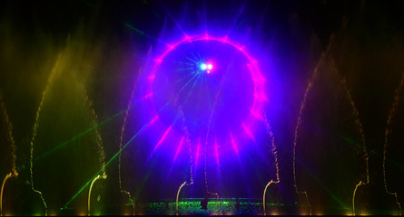 Colorful water fountains. Beautiful laser and fountains show. Large multi colored decorative dancing water jet led light fountain show at night. Dark background.