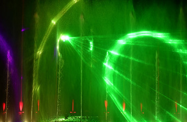 Colorful water fountains. Beautiful laser and fountains show. Large multi colored decorative dancing water jet led light fountain show at night. Dark background.