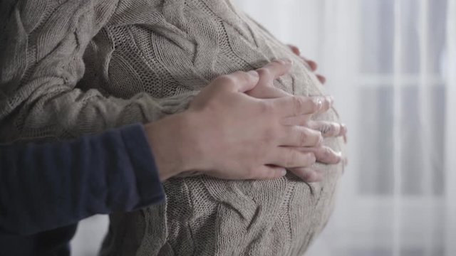 Close-up of male and female Caucasian hands caressing pregnant belly. Young family expecting for family replenishment. Pregnancy, gestation, expectant.