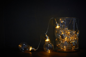 Glass vase filled with luminous bulbs on a wooden table, holiday concept