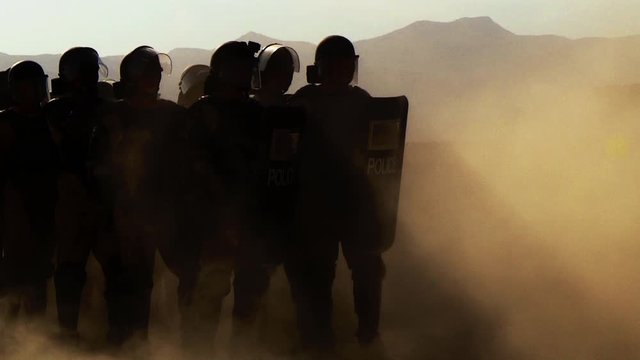 Police with shields and batons lined up in order of battle, dust and sand picks up the wind, contour lighting.