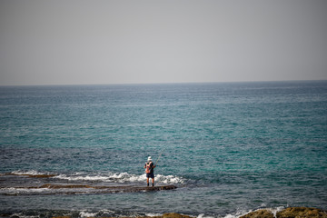 A man fishing in the ocean with his back.