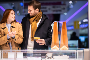 beautiful lovely cute couple in shopping mall together, decided to buy jewelry for woman, man holding discount card in hands going to buy ring