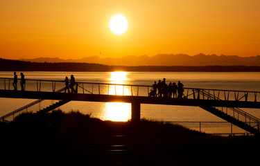 Families taking a sunset stroll over a pier at Chambers Bay Park and Puget Sound