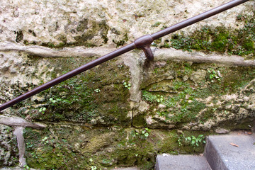 Close-up of a metal railing at a medieval stone staircase covered with green moss, selective focus