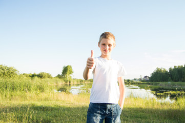 A teenage boy shows a thumbs up. The child stands in nature and smiles. Summer nature. Sunny day.