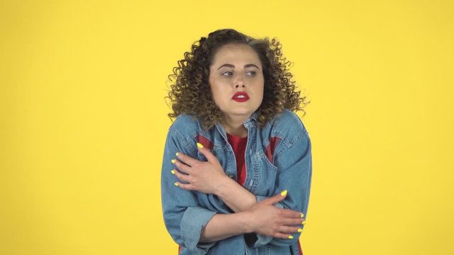 Beautiful girl froze and trying to keep warm on yellow background at studio, slow motion.