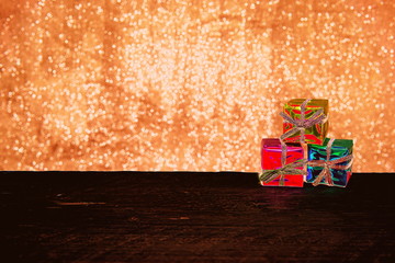 Gift Wrapped Presents on a Product Display Shelf, Showing the Boxes Bow Tied with Multi Coloured Seasonal Tinsel and Foil, on a Plank of Pine Wood with a Bokeh Background.