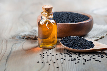 glass bottle of black cumin seeds essential oil , Nigella Sativa in spoon on wooden background. Organic herbal medicine for many diseases, black cumin