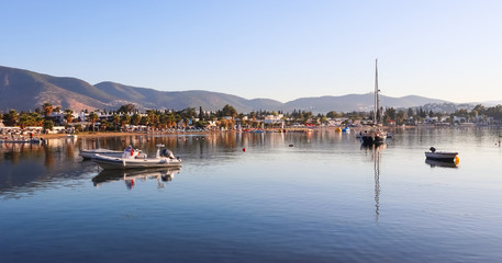 Fototapeta na wymiar Beautiful bay with calm water, sandy beach, boats and yachts. Small town and green mountains on the coast of the Aegean sea