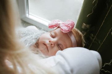 a newborn baby sleeps in the arms of a girl. A little girl with a pink bow on her head. Sleeping baby.