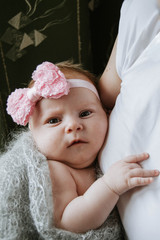 little baby in my mother's arms. A newborn girl with a pink bow on her head. Serious baby