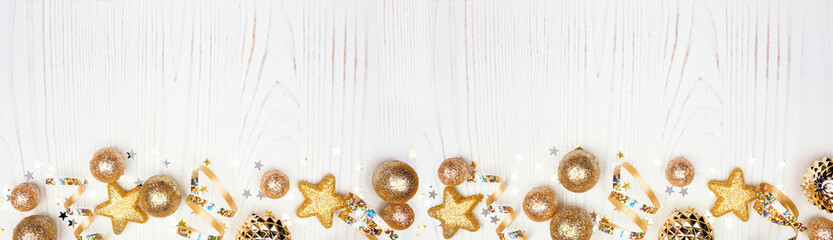 New Years Eve border banner of confetti, streamers and gold decorations. Top view over a white wood background.