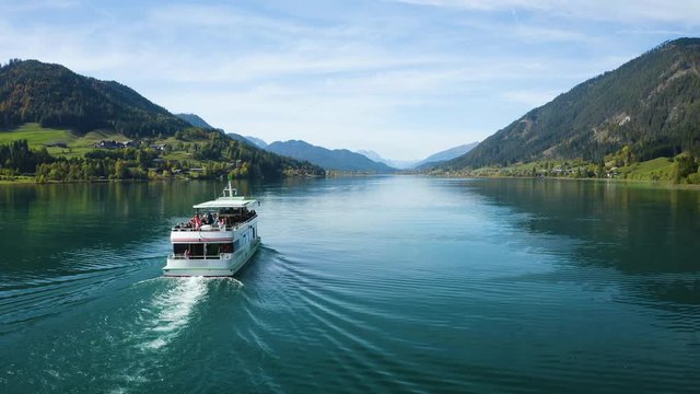 Austria mountain lake aerial panoramic view. The ship is floating on the lake. Drone drone ascend over the ship. Alpine field on coast lake.