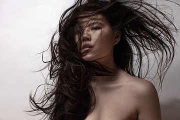 Beautiful Asian model with streamed dark hair on bright background