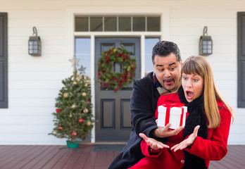 Young Mixed Race Couple Exchanging Gift On Front Porch of House with Christmas Decorations