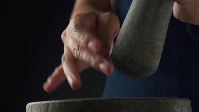 Hand of chef is sprinkling black peppercorns in a stone mortar with a pestle for grinding in the kitchen