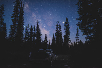 Truck with Milky Way above behind pine trees
