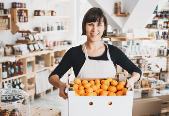 Female with cardboard box of tangerines in zero waste shop.