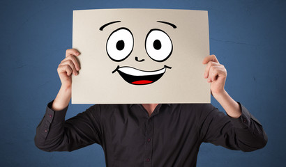 Young student holding a paper with laughing emoticon in front of his face