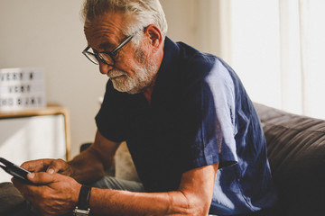 Senior man sitting alone for relaxation and playing game on smart phone in home.