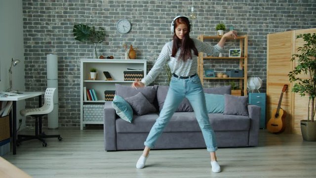 Pretty Young Woman In Wireless Headphones Is Dancing In Apartment Having Fun Alone At Home Wearing Casual Clothing And Shoes. People And Activities Concept.