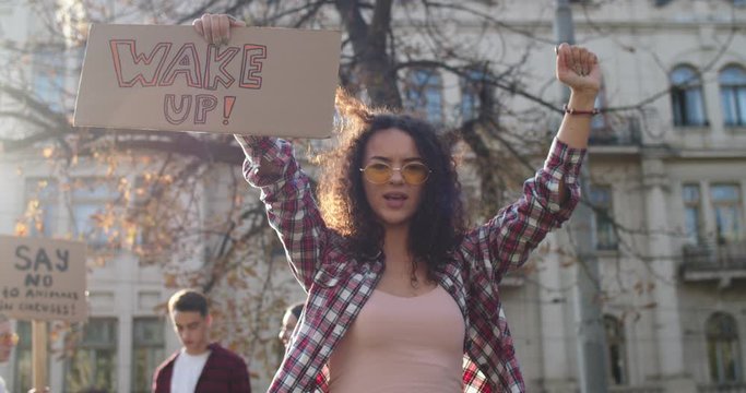 Beautiful young Caucasian woman with curly hair and in sunglasses fighting as the climate change activist at the demonstration with a banner "Wake up". Outdoor.