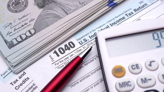 USA Tax form 1040, pen, dollar bills, and calculator. High angle view.