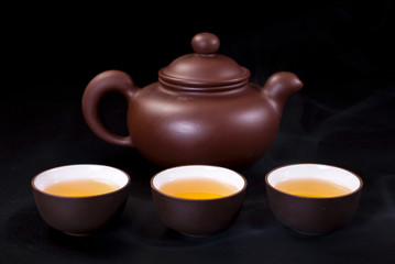 Chinese clay teapot and ceramic tea cups on a black background.