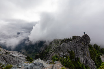 Adventurous Man Standing on top of a rugged rocky mountain during a cloudy summer morning. Taken on Crown Mountain, North Vancouver, BC, Canada.