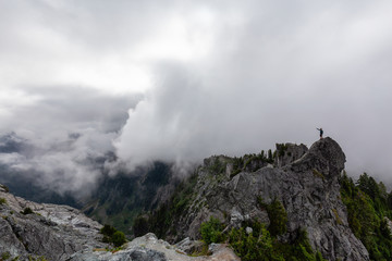 Adventurous Man Standing on top of a rugged rocky mountain during a cloudy summer morning. Taken on Crown Mountain, North Vancouver, BC, Canada.