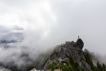 Adventurous Man Standing on top of a rugged rocky mountain during a cloudy summer morning. Taken on Crown Mountain, North Vancouver, BC, Canada.