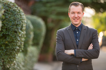 Happy young handsome businessman smiling with arms crossed outdoors