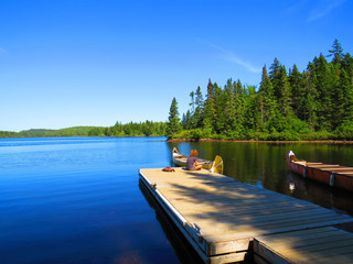 Young woman sitting near a Canadian lake. Canoe resting by the calm water  Mauricie National Park,...