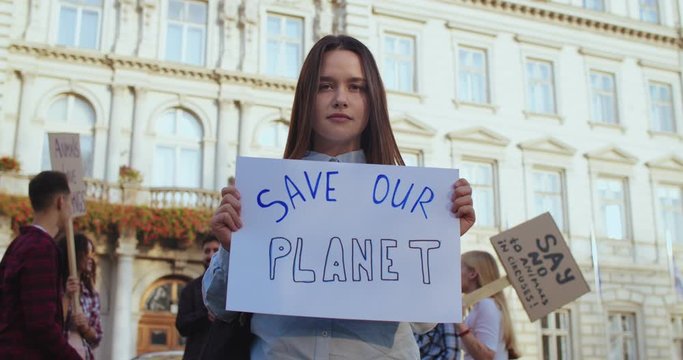 Portrait of the young beautiful Caucasian girl student standing outdoors at the governmental building with a table "Save our planet".