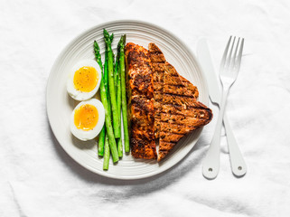 Healthy diet lunch - baked salmon, boiled soft eggs, asparagus and wholegrain bread on a light background, top view