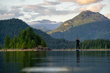 Adventurous Girl on a Paddle Board is paddling in a calm lake with mountains in the background...