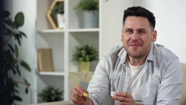 Waist Up Shot Of Cheerful Middle Aged Man Eating French Fries And Chicken With Sauce And Watching Comedy Movie On TV In The Living Room